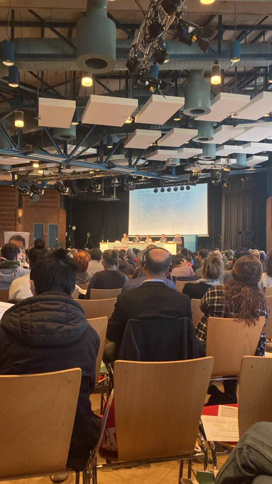 A picture of the conference hall, with 4 speakers on stage together with the moderator. Around 1300 people are in attendance.