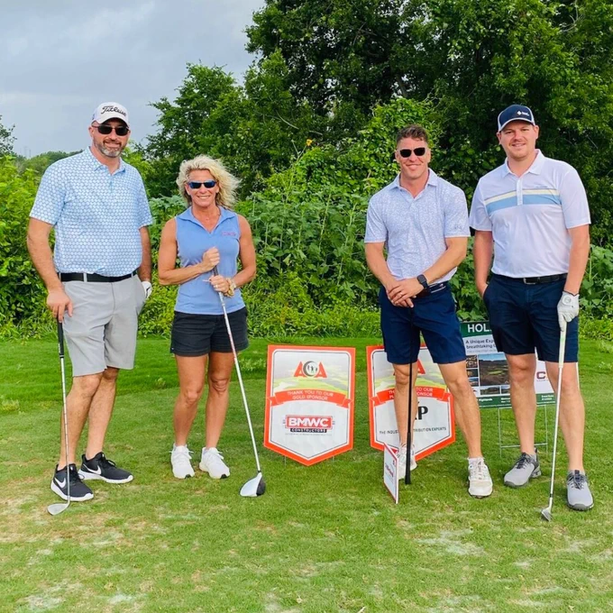 Seth Alford posing with BMWC Gold Sponsor sign at American Cleft Palate Craniofacial Association golf outing. Four people holding putters. 