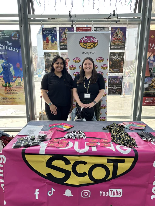 A photo of two women standing behind a Young Scot branded table smiling at the camera