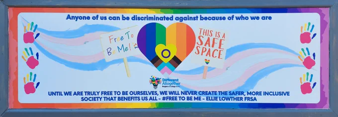 Free To Be Me mural (on the exterior wall of ARC), with trans colours, hand prints, and a placard illustration stating 'This is a safe space'. Text on the mural reads 'Any one of us can be discriminated against because of who we are. Until we are truly free to be ourselves, we will never create the safer, more inclusive society that benefits us all - #FreeToBeMe' - Ellie Lowther FRSA