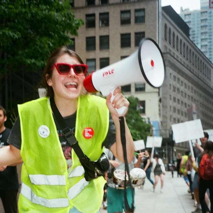 film photo of an Insider Union strike captain yelling into a white and red blow horn outside the Insider office