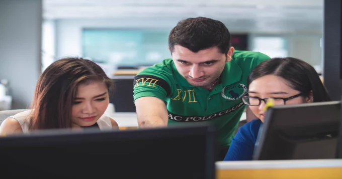A man and two women collaborating, staring at computer screens.
