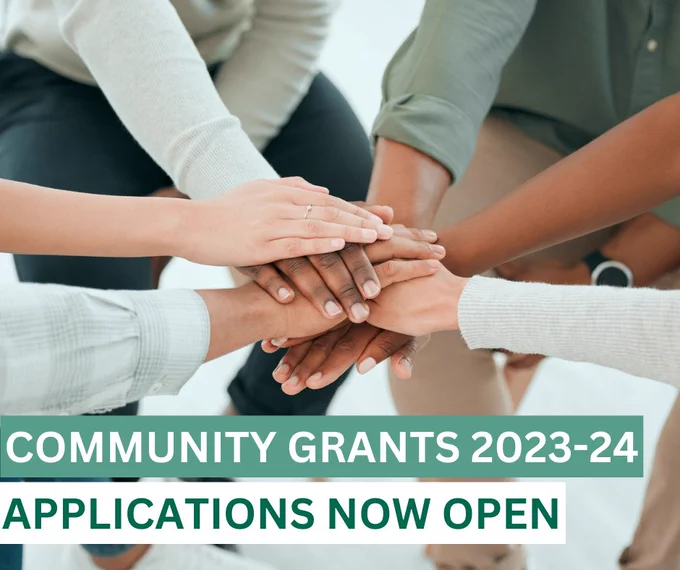 An image showing a group of people putting their hands together with the words "Comunity Grants 2023-2024, applications now open" overlayed. 