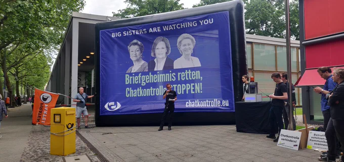 Blick in die Demo mit großem Banner "Bis sisters are watching you" - Briefgeheimnis retten, Chatkontrolle stoppen! Mit den Bildern von Faeser, Johannson und Von der Leyen. 