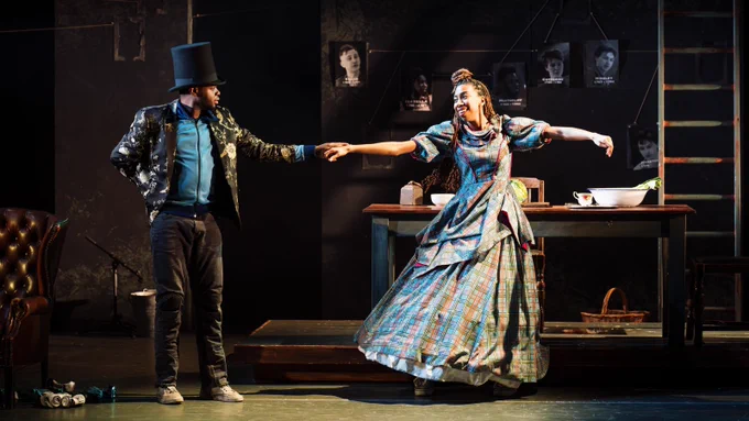 A woman holds her hand out to a man wearing a top hat. They appear to be dancing on stage. 