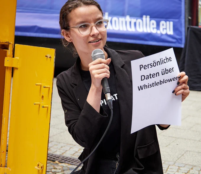 Anne hält neben dem offenen Briefkasten einen geöffneten Brief, auf dem "Persönliche Daten über Whistleblower" steht. 