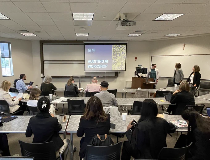 people sitting in a classroom looking at a screen with the words “Auditing AI Workshop”