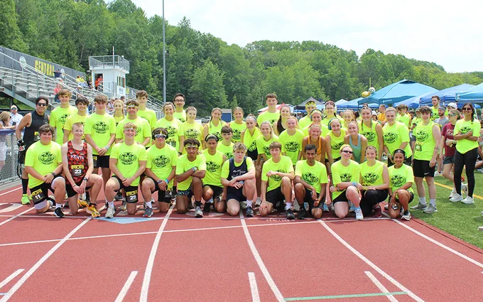 Large group of students on track outdoors, trees, sky, stands