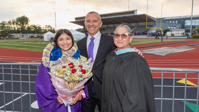 A grad with flowers and superintendent and school board member