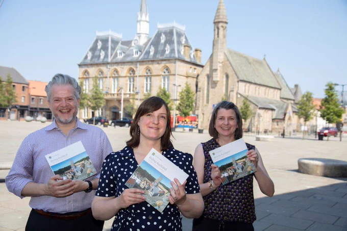 A photograph of three people standing in a line, each holding a book. 