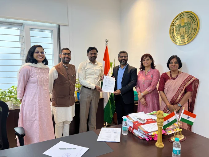 The Raspberry Pi Foundation and Telangana Social Welfare Residential Educational Institutions Society celebrating our partnership. 6 people in an office in front of an Indian flag, 2 people in the middle of the photo holding a signed partnership agreement.
