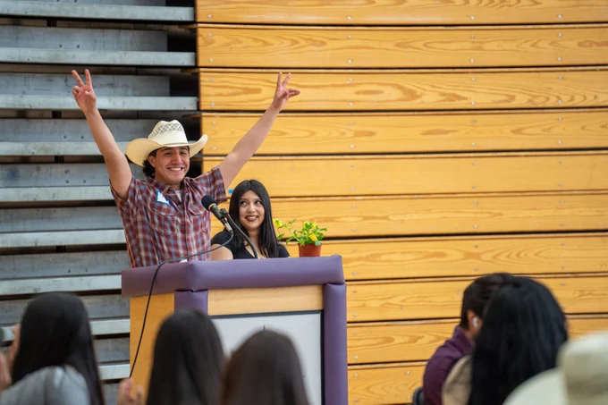 A student throws up peace signs as he speaks to a group