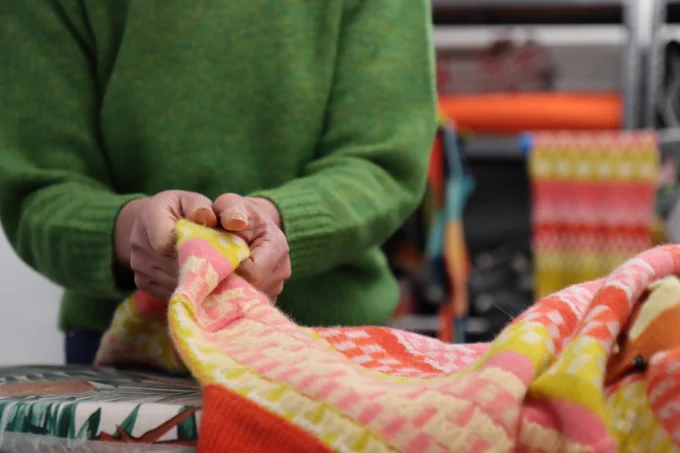 A figure wearing a green knit jumper handles a brightly patterned textile.