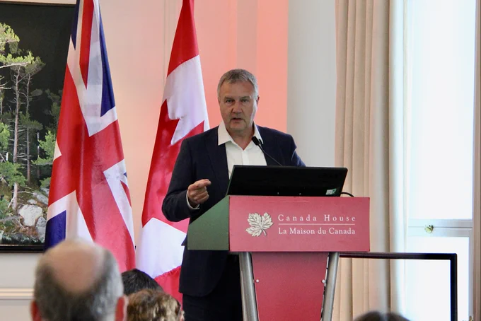 Tim Mordan giving a speech from a Canada House branded podium with Canadian and UK flags in the background.