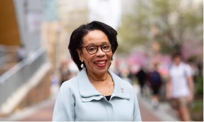 JoAnne Epps stands in a blue powdered jacket, smiling, with Polett Walk behind her, blurred out.