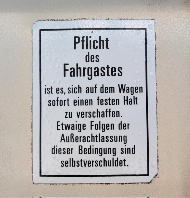 Ein Schild aus der Duisburger Stadtbahn mit folgendem Text: Pflicht des Fahrgastes ist es sich auf dem Wagen sofort einen festen Halt zu verschaffen. Etwaige Folgen der Außerachtlassung dieser Bedingung sind selbstverschuldet.