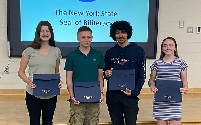 Four students holding certificates, smiling