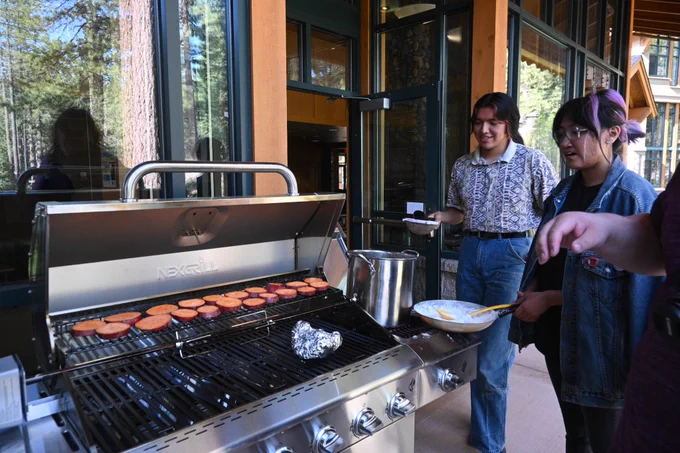 two people cooking at a grill with yams and metal pot