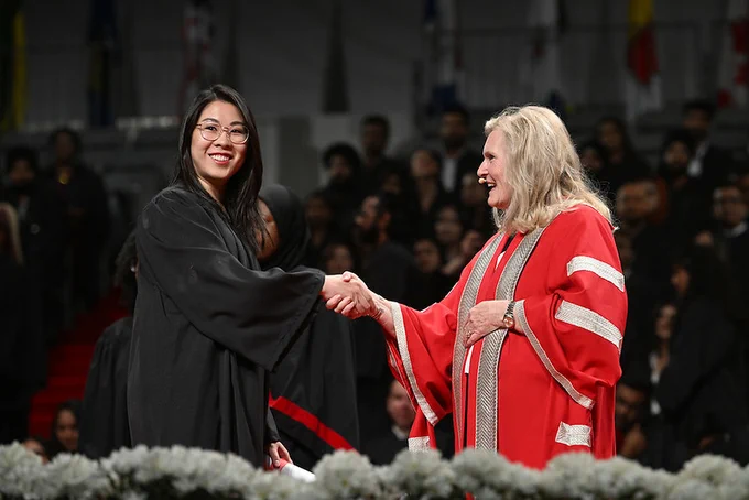 York President Rhonda Lenton shakes hands on stage during the School of Continuing Studies graduation ceremony.