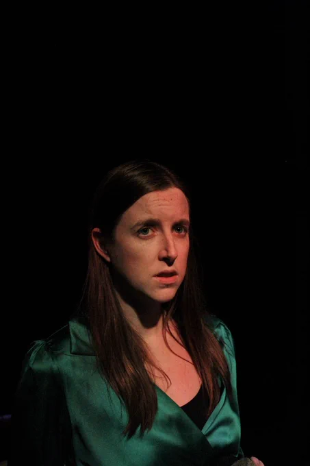  Brontë, a young white woman with long light brown hair and a green dress, looking despondent.