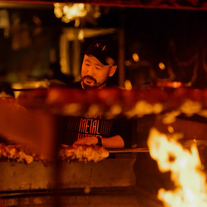 Mona's head chef attends to the meat being cooked outside Dark Mofo's Winter Feast at the Heavy Metal Kitchen stall. Out of focus in the foreground is more meat and fire.