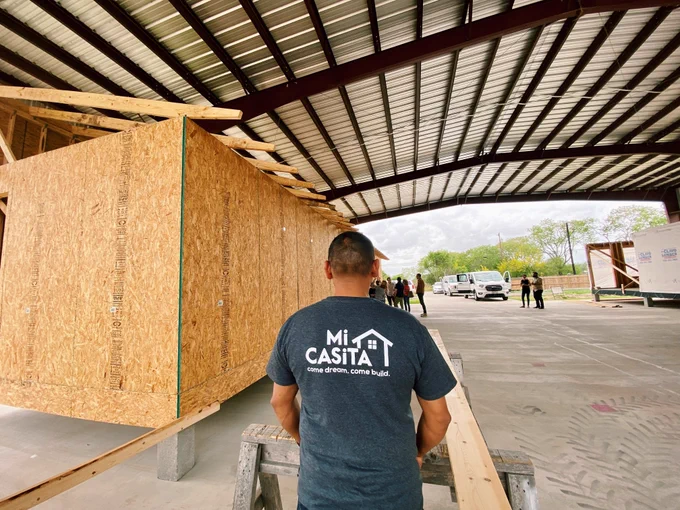 MiCASiTA homes under construction at The Farm. A worker stands face away from the camera. Thedark  gray T-shirt they are wearing shows the MiCaSiTa logo proudly on the back.