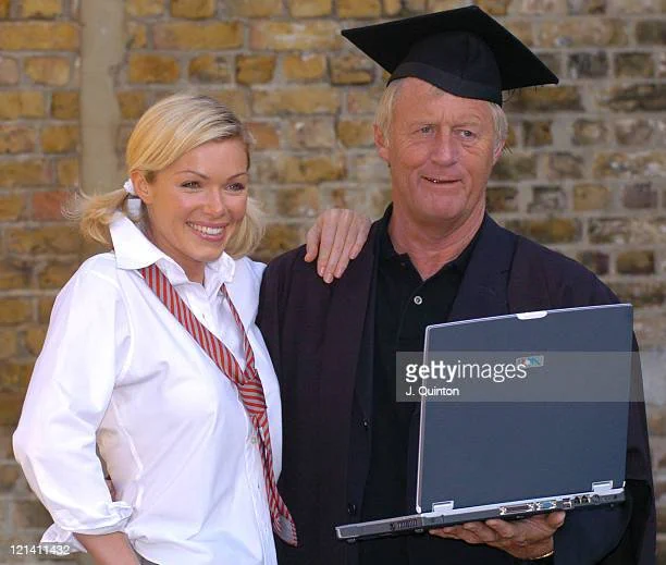 In the same outfits as the previous photo, Nell McAndrew has her hand on Chris Tarrant's shoulder. He is holding a laptop.