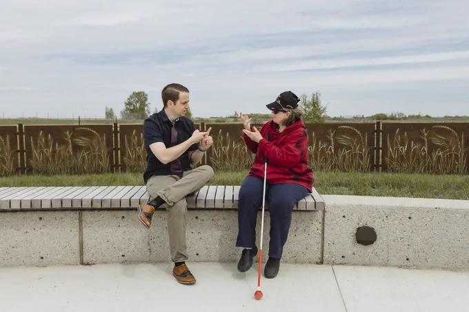 A DBCS manager and client sit outside and have a conversation using American Sign Language. 