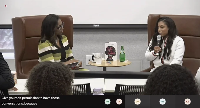 Within an auditorium setting, a moderator engages in conversation with Mindy Harts. Seated across from each other, they are positioned around a central round table, upon which Mindy's book, titled "Within Right," is prominently displayed.