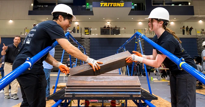 Two students from the UC San Diego steel bridge team load the bridge with weights for a loading test. 