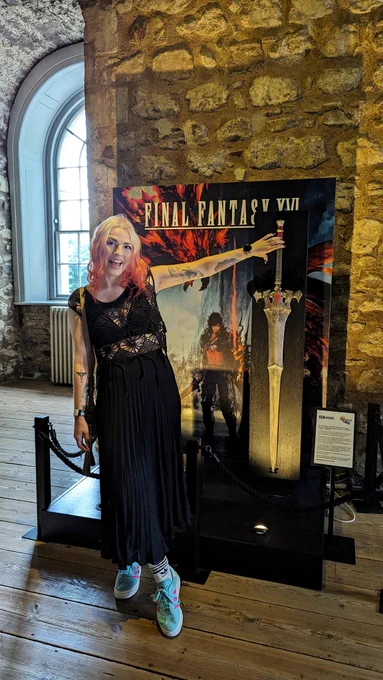 Picture of me reaching for Clive's Invictus sword from Final Fantasy XVI that is displayed in the tower of London. 