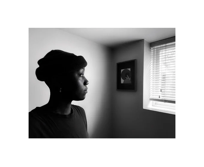 A black and white photo of a person looking out a window. Artwork by Alicia-Zayne Besentie.