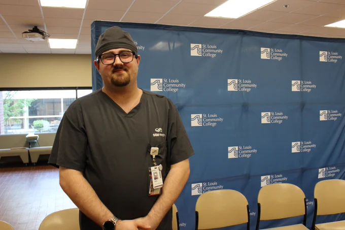 Dallin Lake wears scrubs while posing in front of a blue STLCC backdrop.