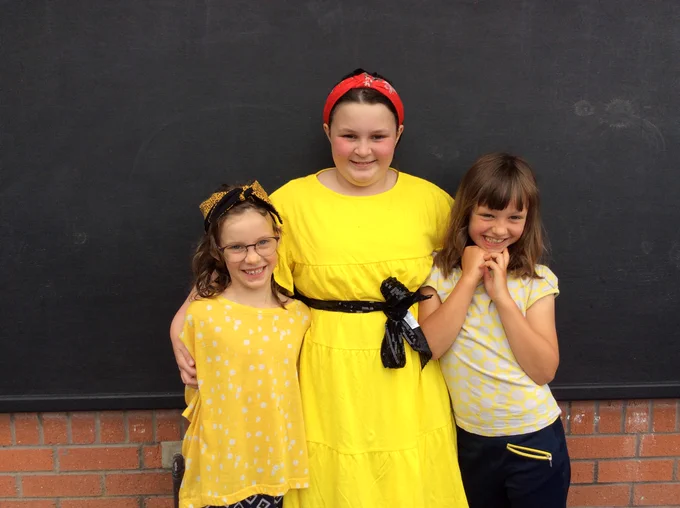 A photo of three young girls, all wearing yellow, smiling at the camera.
