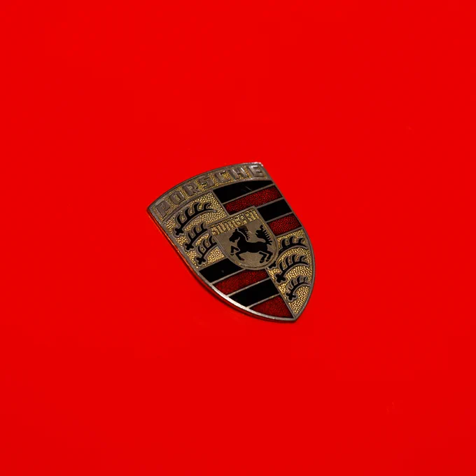 Close-up of a Porsche badge on a red bonnet.