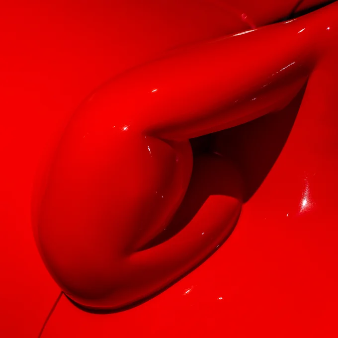 Close up of a side-mirror on a car. The exterior of the mirror is thick, red and bulging making the mirror hard to see. 