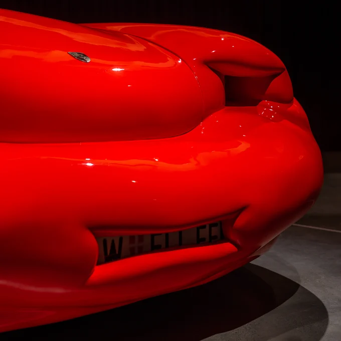 Close- up of the front of a red Porsche that has a red, thick exterior. The number plate and headlights are partially covered.