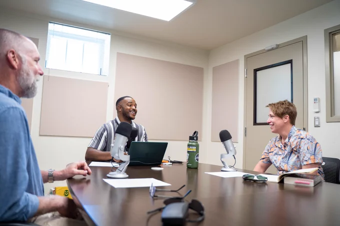 From left, Matt Hickey, Avery Martin, and Kari Dockendorff record a podcast in front of microphones.