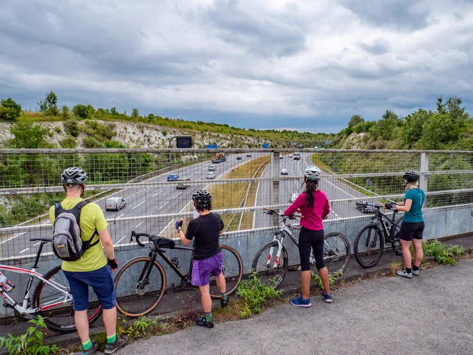 Four cyclists stands on a bridge crossing over a motorway