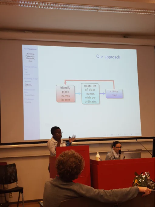 A group of people infront of a presentation in a lecture hall. Slide title: Our approach