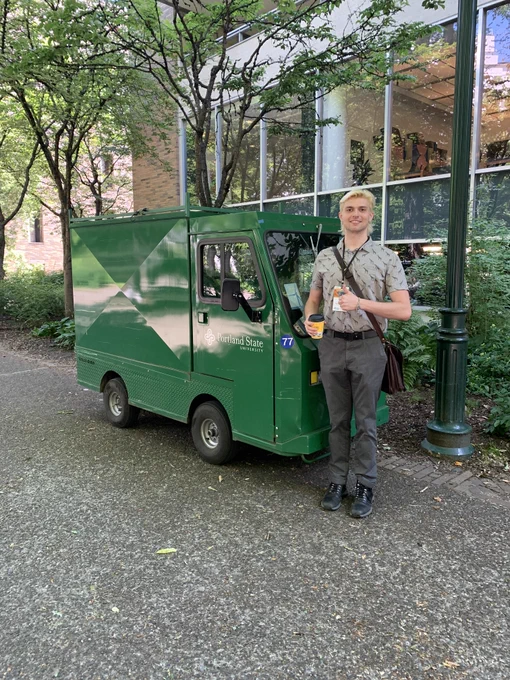 OPCD planning and data analyst Phillip Carnell posing next to a green mini vehicle that says "Portland State University" on it.