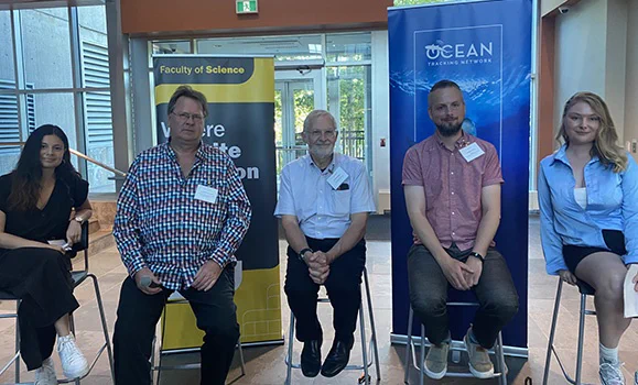 Five panelists sit on stools ahead of a panel discussion
