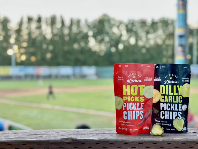 The Hot Picks & Dilly Garlic Pickle chips on display with a Pickles game happening behind them