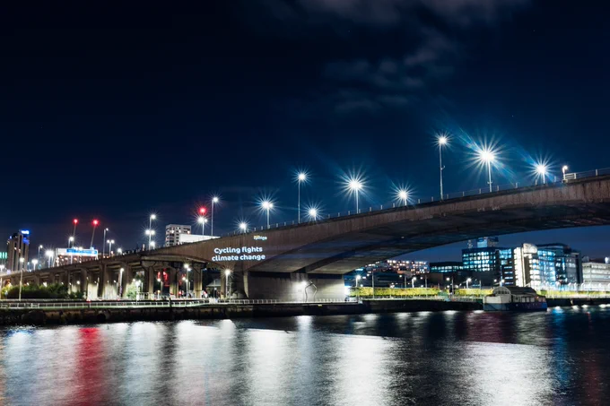 Projection with text "Cycling fights climate change" on a road bridge in Glasgow