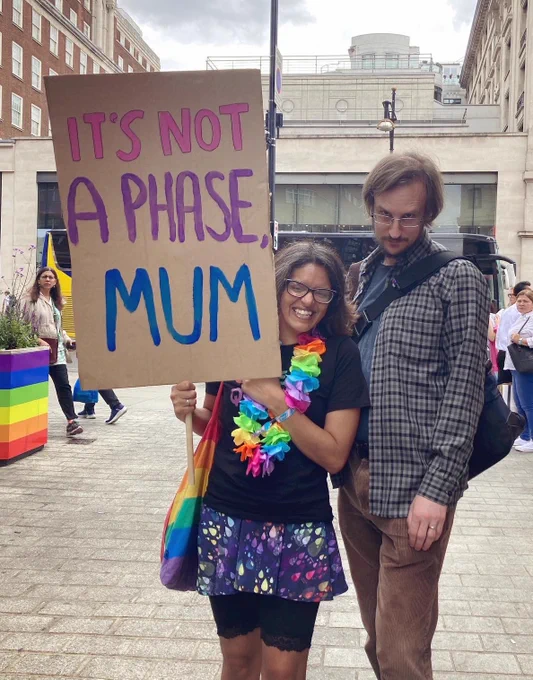 Me and A smiling at the camera with a placard in bi colours reading “IT’S NOT A PHASE, MUM”