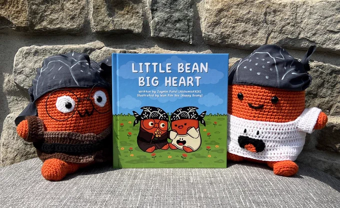 Ren (left) and Hikari (right) crochet plushies accompanied by a hardcover copy of Little Bean Big Heart by AlchemistXIX and Happy Beany 🫘💖