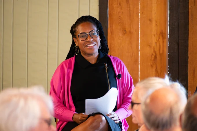 Dr. Conra Gist smiles and sits on a chair speaking to legislators.