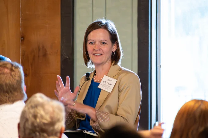 Dr. Erin Crisp gestures and speaks to an audience of legislators.