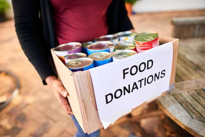 Photo showing a person carrying a box with tinned goods labelled "Food Donations"