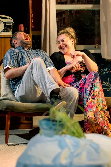 Steven George and Helen Fox laughing together on the sofa in the living room.